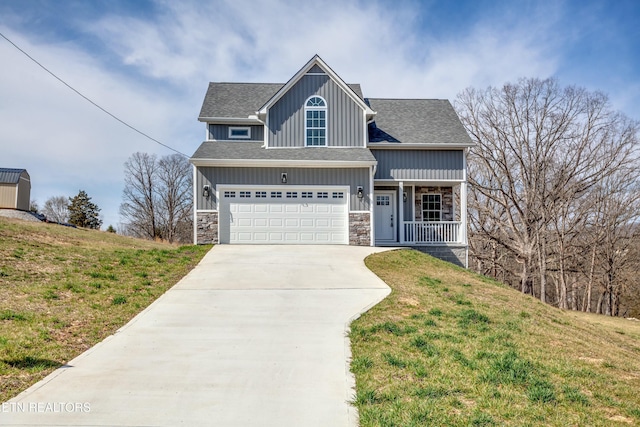 view of front of home featuring a front yard, driveway, covered porch, stone siding, and board and batten siding