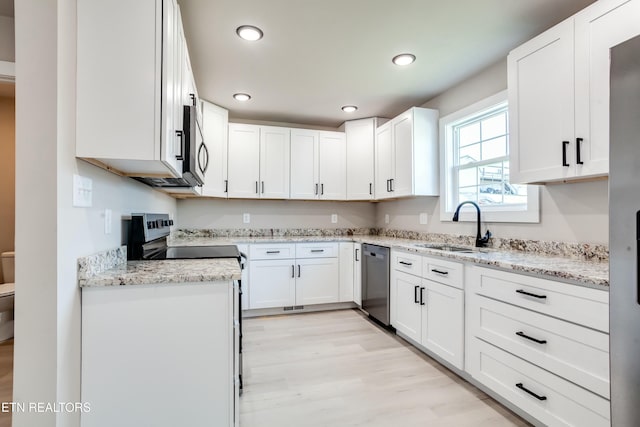 kitchen with light stone countertops, a sink, light wood-style floors, appliances with stainless steel finishes, and white cabinetry