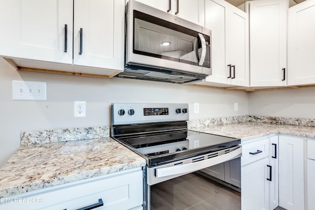 kitchen with wood finished floors, white cabinets, light stone countertops, and stainless steel appliances