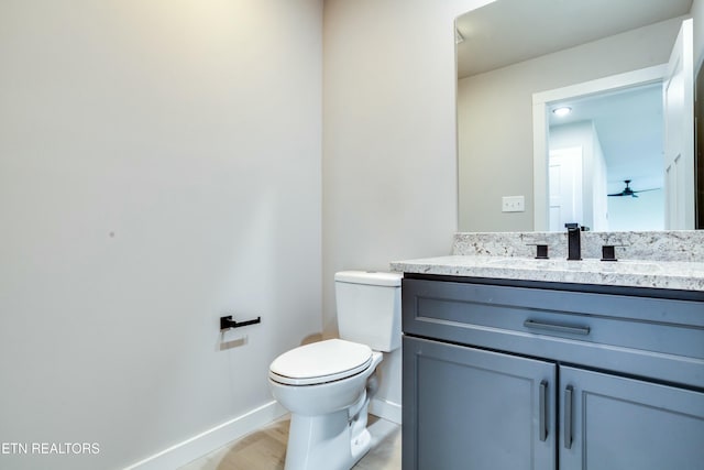 half bathroom featuring baseboards, toilet, wood finished floors, vanity, and a ceiling fan