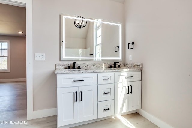 full bathroom with wood finished floors, baseboards, an inviting chandelier, double vanity, and a sink