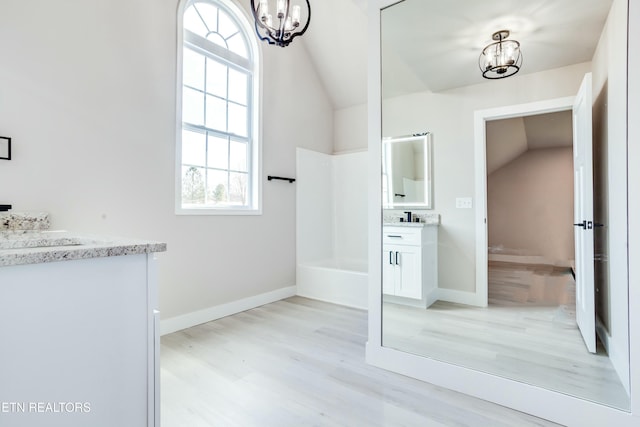 full bath featuring baseboards, a chandelier, vaulted ceiling, wood finished floors, and vanity