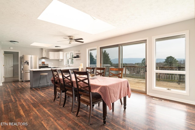 dining room with dark wood-type flooring, a skylight, and a textured ceiling