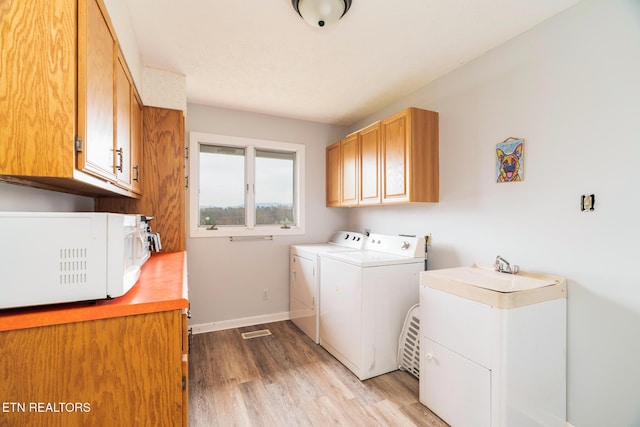 laundry room featuring washer and clothes dryer, a sink, cabinet space, light wood finished floors, and baseboards