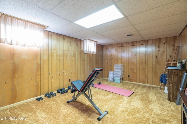 exercise area featuring a paneled ceiling, wooden walls, and carpet flooring