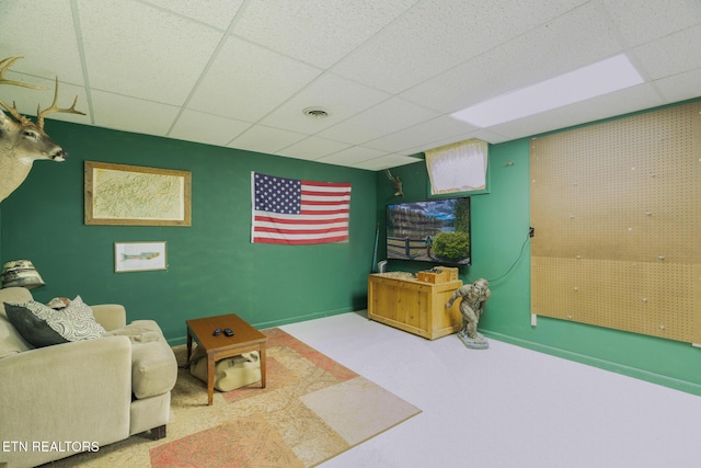 living area featuring an accent wall, carpet, visible vents, and a drop ceiling