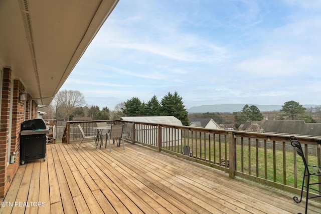 wooden terrace with outdoor dining space, a mountain view, and a grill