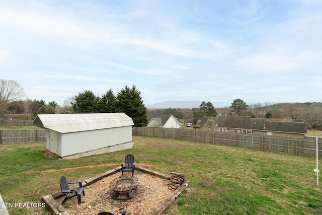 view of yard with an outbuilding, a fenced backyard, a storage shed, and an outdoor fire pit