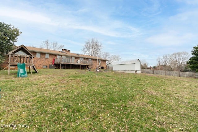 view of yard with a playground, an outbuilding, a deck, and fence