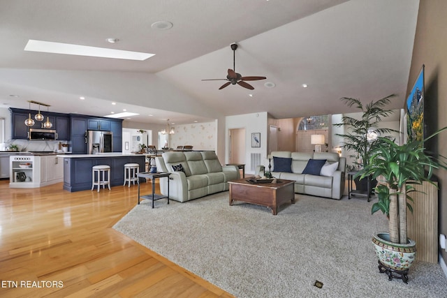 living room featuring vaulted ceiling with skylight, recessed lighting, light wood finished floors, and ceiling fan