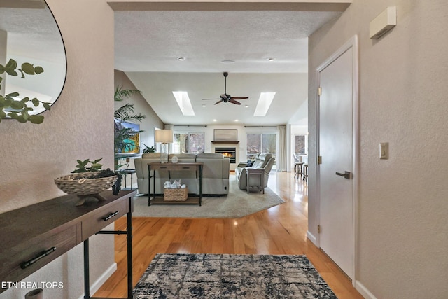 interior space featuring lofted ceiling with skylight, wood finished floors, a lit fireplace, a textured wall, and a textured ceiling