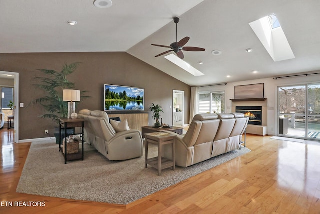 living room with a glass covered fireplace, wood finished floors, vaulted ceiling with skylight, and a healthy amount of sunlight