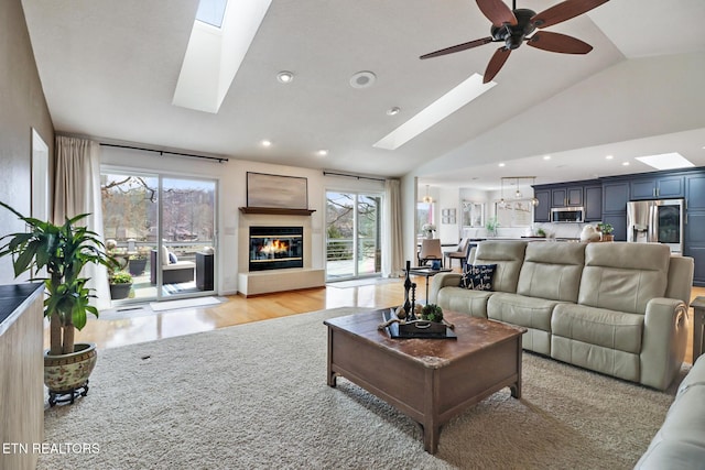 living area featuring light wood finished floors, lofted ceiling with skylight, recessed lighting, a glass covered fireplace, and a ceiling fan