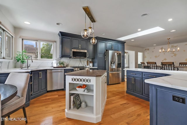 kitchen featuring a kitchen island, open shelves, a sink, appliances with stainless steel finishes, and a notable chandelier