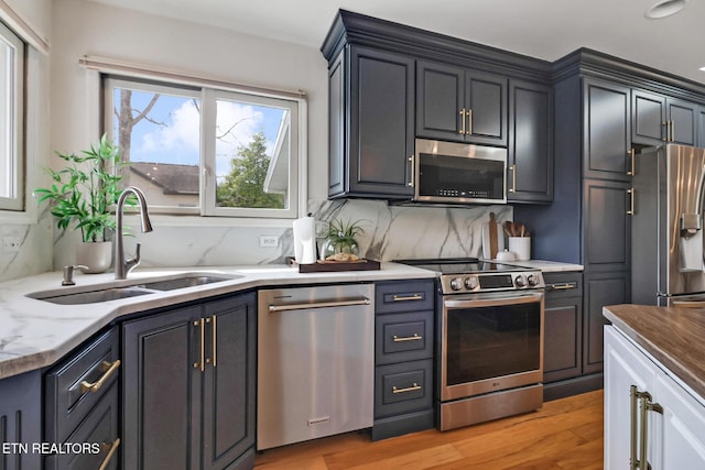 kitchen featuring a sink, backsplash, stainless steel appliances, light wood finished floors, and light stone countertops