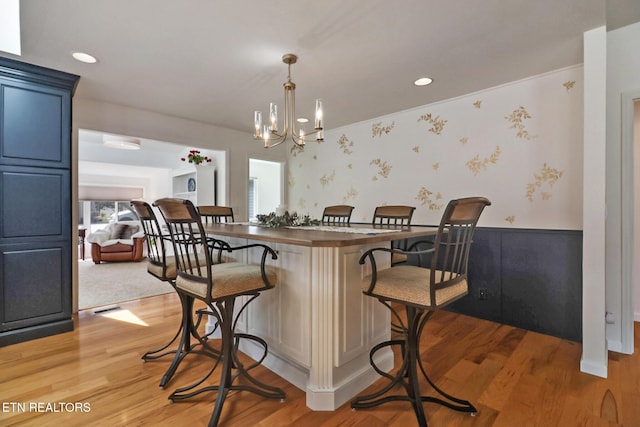 kitchen featuring a wainscoted wall, light wood finished floors, wallpapered walls, a breakfast bar, and blue cabinetry