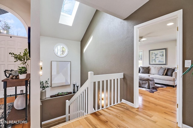 interior space with lofted ceiling with skylight, wood finished floors, a ceiling fan, and a textured wall