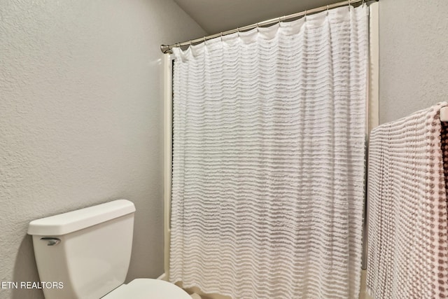 bathroom featuring curtained shower, toilet, and a textured wall