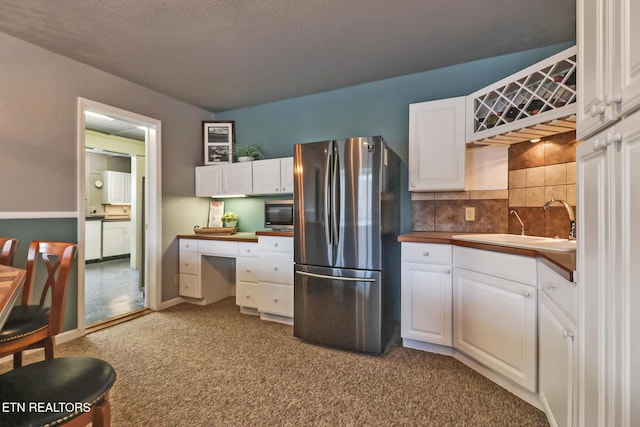 kitchen featuring tasteful backsplash, carpet, freestanding refrigerator, white cabinets, and a sink