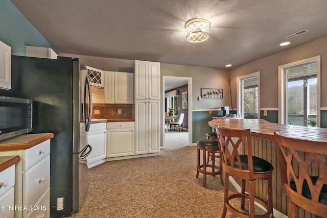 dining room with visible vents, light carpet, recessed lighting, a textured ceiling, and a dry bar