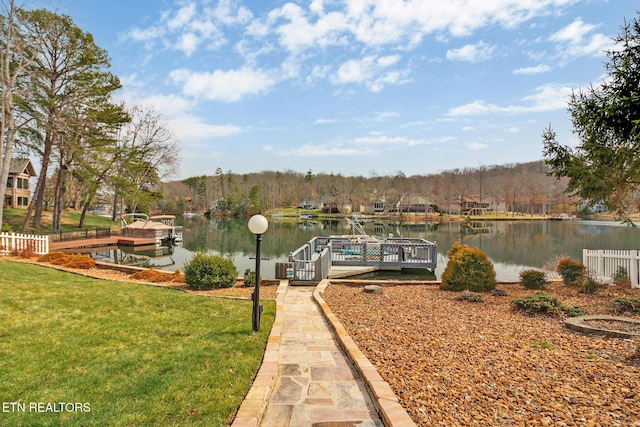 view of dock featuring a water view, a lawn, and fence