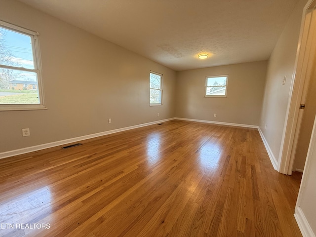 spare room featuring visible vents, baseboards, a textured ceiling, and wood finished floors