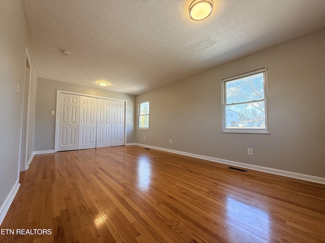 unfurnished bedroom with visible vents, baseboards, wood finished floors, a closet, and a textured ceiling