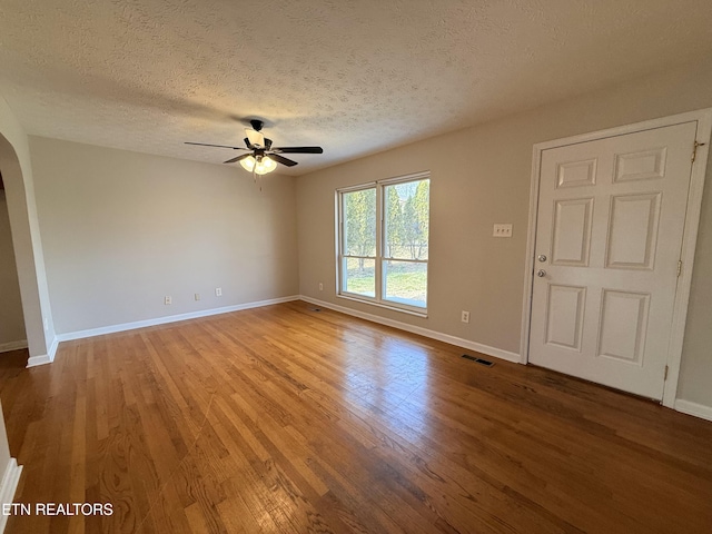 empty room featuring wood finished floors, baseboards, visible vents, arched walkways, and ceiling fan