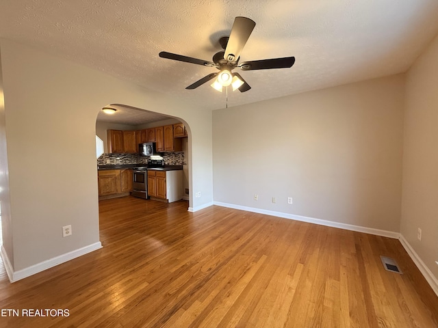 unfurnished living room featuring wood finished floors, visible vents, baseboards, arched walkways, and ceiling fan