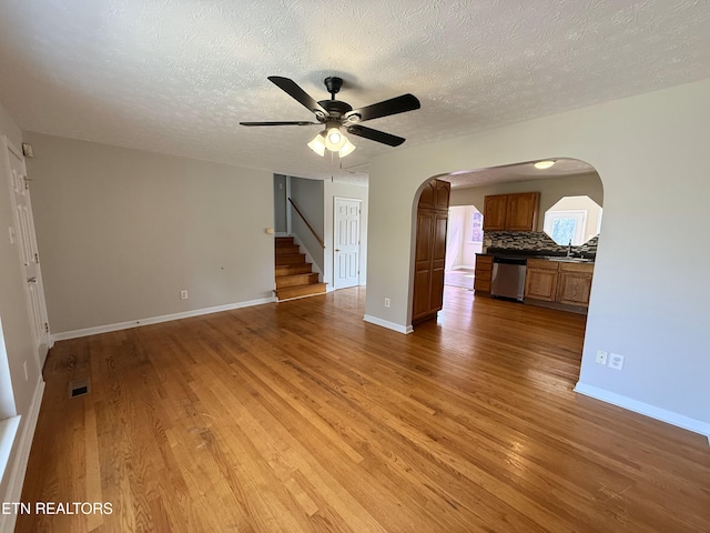 unfurnished living room featuring a sink, arched walkways, light wood-style floors, and ceiling fan