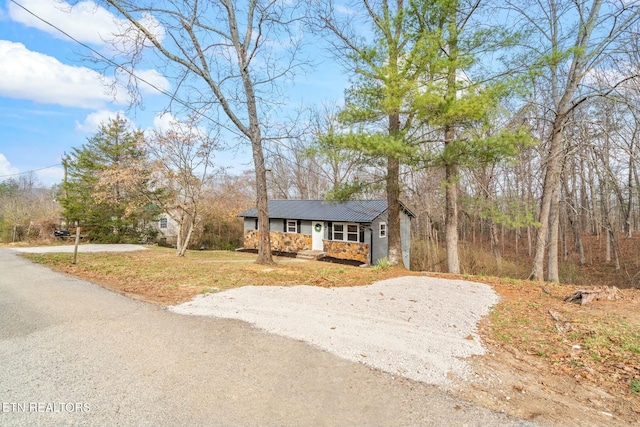 view of front of property with a front yard, covered porch, stone siding, and driveway