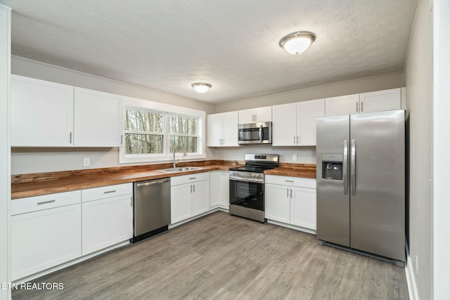 kitchen with a sink, wooden counters, appliances with stainless steel finishes, and white cabinets