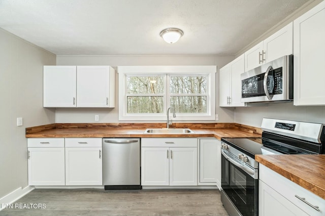 kitchen featuring light wood-style flooring, a sink, appliances with stainless steel finishes, white cabinets, and wooden counters