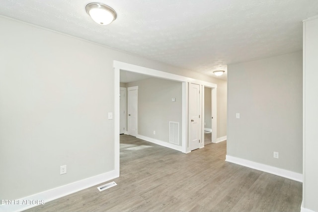 unfurnished room featuring visible vents, baseboards, a textured ceiling, and wood finished floors