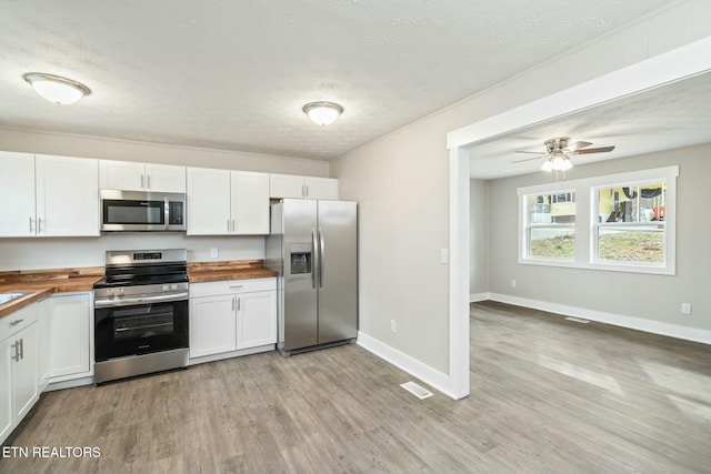 kitchen featuring light wood finished floors, white cabinetry, stainless steel appliances, and wood counters