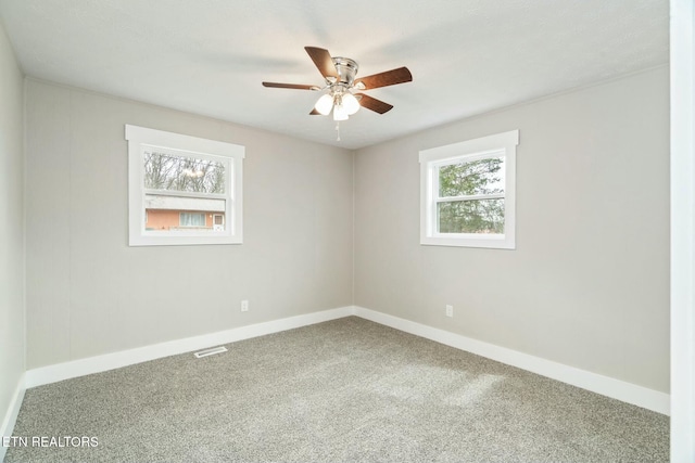 carpeted spare room featuring baseboards, visible vents, and ceiling fan