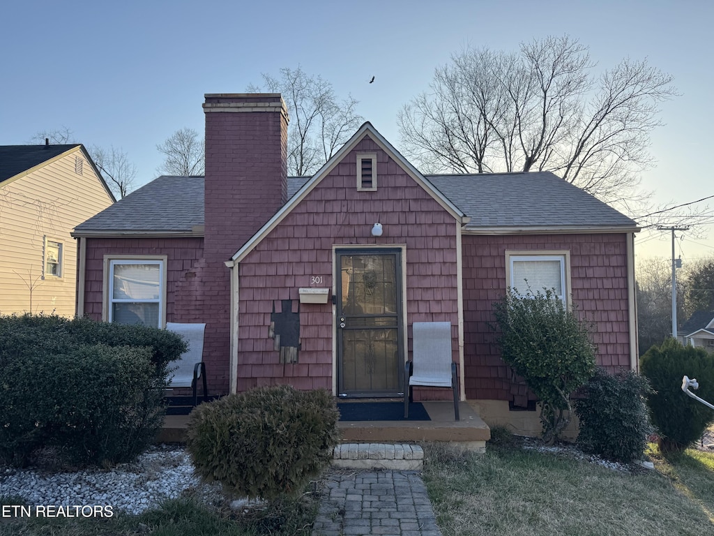 bungalow-style house featuring a chimney and a shingled roof