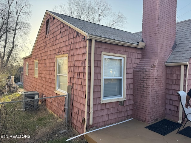 view of side of home with cooling unit, fence, a chimney, and a shingled roof