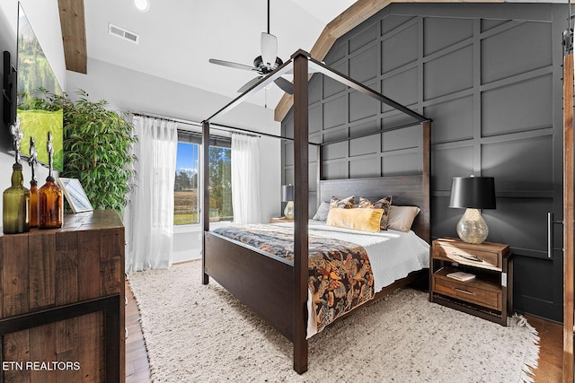 bedroom featuring a decorative wall, ceiling fan, visible vents, and wood finished floors