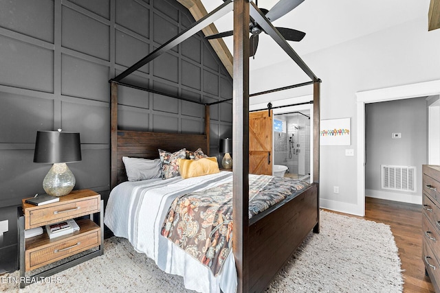 bedroom with visible vents, baseboards, a barn door, wood finished floors, and a decorative wall
