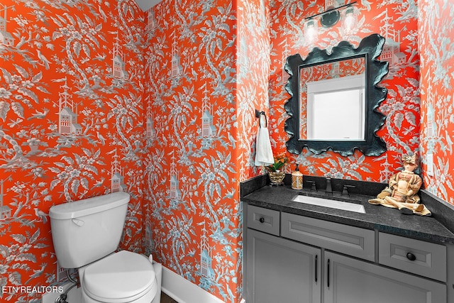 half bathroom with toilet, vanity, and wallpapered walls