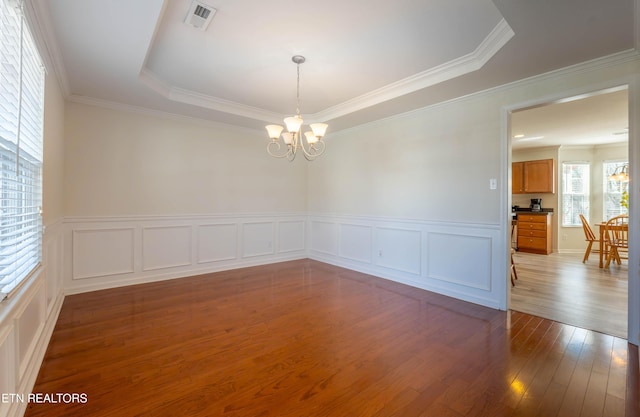 spare room featuring a notable chandelier, crown molding, a raised ceiling, wood finished floors, and visible vents