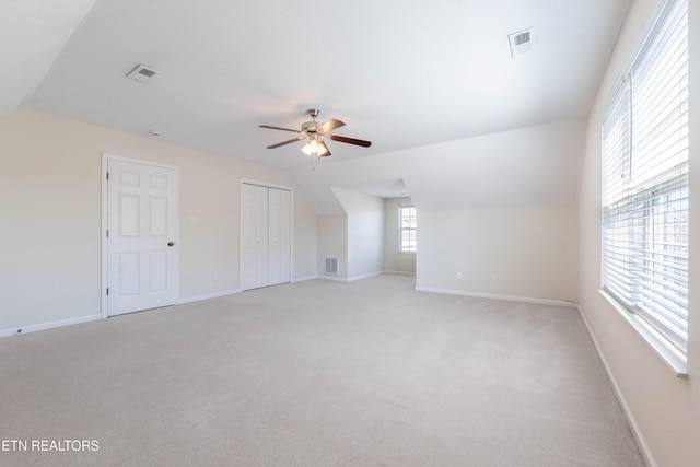 interior space featuring light colored carpet, lofted ceiling, ceiling fan, and visible vents