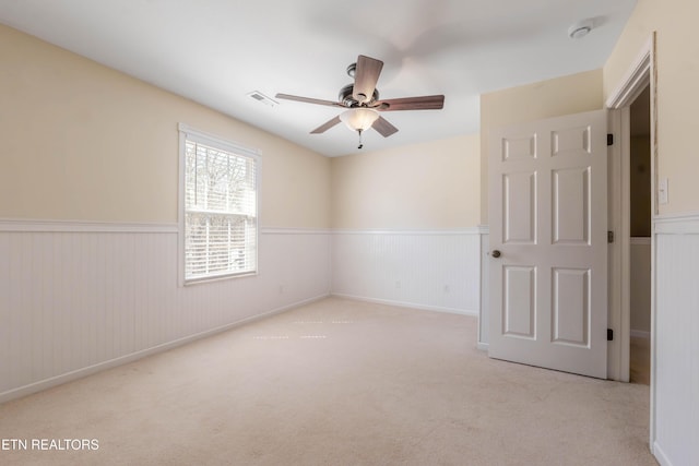 carpeted empty room featuring ceiling fan, visible vents, and wainscoting