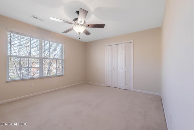 unfurnished bedroom featuring light colored carpet, baseboards, ceiling fan, visible vents, and a closet