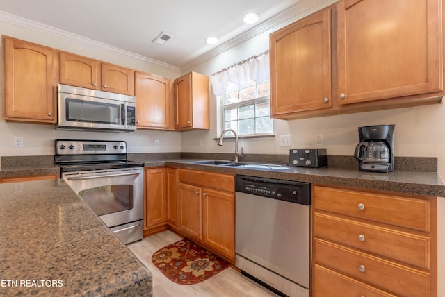 kitchen with crown molding, a sink, light wood-style flooring, stainless steel appliances, and visible vents