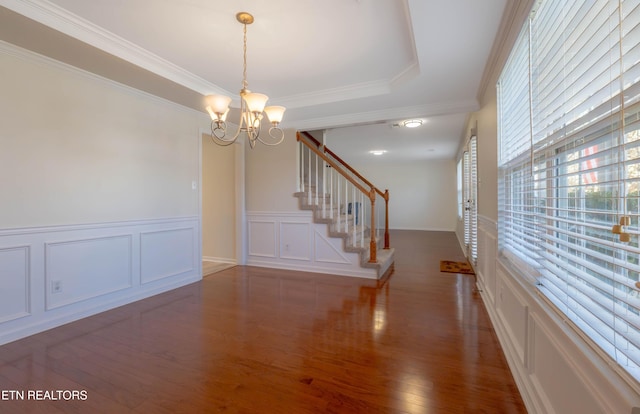 interior space with crown molding, wood finished floors, a raised ceiling, and a chandelier