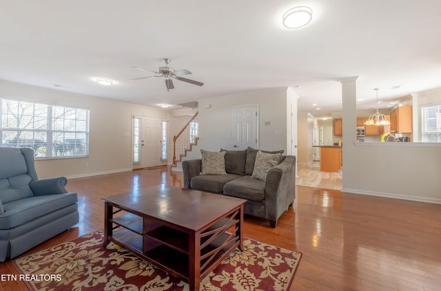 living area with stairway, light wood-style flooring, baseboards, ceiling fan, and ornamental molding