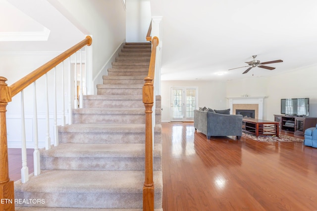 stairs featuring a fireplace, crown molding, ceiling fan, and wood finished floors