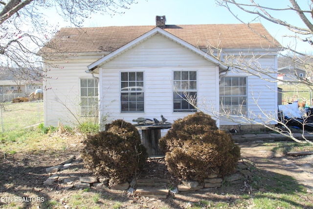 back of house featuring roof with shingles and a chimney